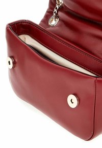 Bolso de cuero rojo con una textura suave, que presenta una correa de cadena, herrajes dorados y un bolsillo frontal con un cierre a presión metálico.