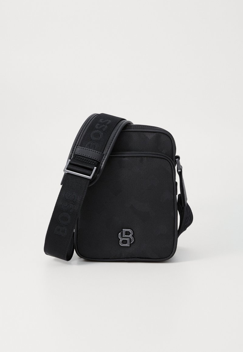 Black crossbody bag with a sleek design, made of textured fabric. Features a bold logo and adjustable strap with branding. Compact and modern.