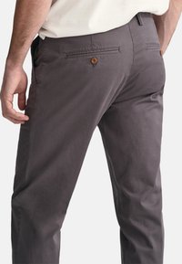 Grijze katoenen broek met een gladde textuur, voorzien van een knoopzak aan de achterkant en subtiele stikdetails op de tailleband en zoom.