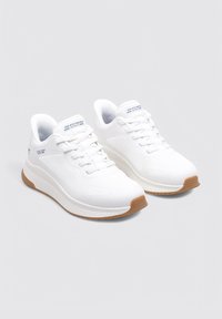 Białe buty sportowe z siateczkową cholewką, wyściełanym kołnierzem i gumową podeszwą. Posiadają sznurowanie z przodu oraz subtelne logo na języku.