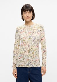 Μακρυμάνικο πουκάμισο από ανοιχτό κρέμα ύφασμα, με πολύχρωμο ουράνιο μοτίβο που περιλαμβάνει αστέρια, λουλούδια και σχέδια που κυκλώνουν την επιφάνεια.