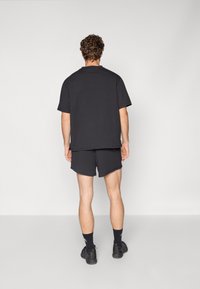 T-shirt en coton noir à manches courtes, assortie à un short noir. Design simple, coupe décontractée, portée avec des chaussettes de sport noires et des chaussures.