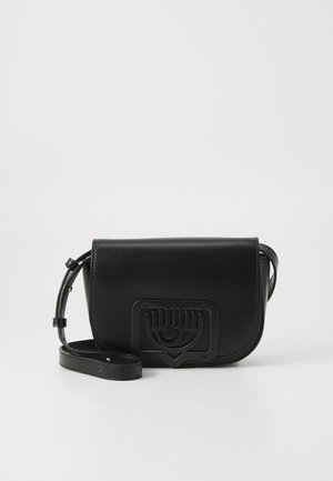 Musta nahkainen olkalaukku, jossa säädettävä hihna ja kohokuvioitu silmän muotoinen kuvio etuklapissa, yksiväristä valkoista taustaa vasten.