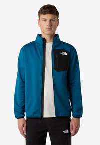 Giacca in pile teal da uomo con colletto alto, tasca sul petto con zip nera e zip nera a contrasto. Tessuto morbido, design leggero.