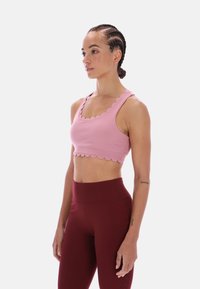Světle růžová sportovní podprsenka s vroubkovanými okraji, jemnou texturou a širokými ramínky, doplněná o vínové legíny s vysokým pasem.