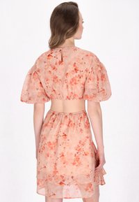 To-delt, blomstrete kjole i blød ferskenfarve, med en cropped top med pufærmer og åben ryg, samt en lagdelt, volangskaft nederdel.