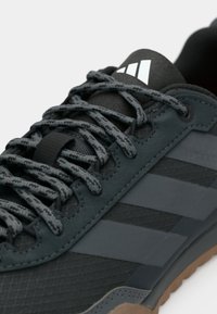 Μαύρο αθλητικό παπούτσι με υφασμάτινη πλέξη και συνθετικά υλικά, γκρι κορδόνια και τρεις χαρακτηριστικές ρίγες σε σκουρότερη απόχρωση.