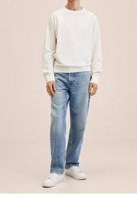 Biała bluza crewneck z prążkowanymi mankietami, zestawiona z jasnoniebieskimi prostymi jeansami i białymi trampkami na neutralnym tle.