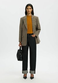 Brūns šaurs pārvalks virs oranžas augšdaļas, kombinēts ar melnām džinsām. Džinsiem ir salocīti piedurknes, un tos papildina melni norādījuma papēži un somiņa.