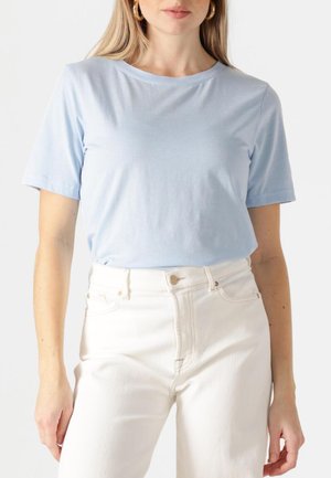  Lichtblauwe korte mouwen T-shirt met een ronde halslijn, met een gladde textuur, gedragen met hoge witte jeans met een knoopaccent.