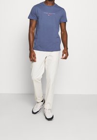 Námořnická modrá bavlněná tričko s logem "Tommy Hilfiger", spárované se smetanovými kalhotami a černobílými atletickými botami.