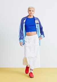 Sportigt outfit bestående av en blå crop top, en ljusblå och marinblå jacka, vit kjol och röda sneakers med randiga strumpor.