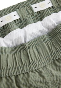 Gröna tygshorts med elastisk midja, med vit nätfoder, platta knappar och synliga söms detaljer.