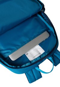 Kék hátizsák belseje, sima, párnázott rekesszel laptopnak, címkével és kontrasztos cipzárszegélyekkel.