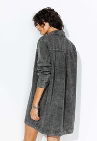 Robe chemise en denim gris, à manches longues, coupe ample, col boutonné, poche poitrine à l'avant, longueur mi-cuisse, et texture légèrement décolorée.