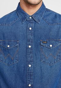Blauwe denim shirt met een kraag, voorkant met drukknoopjes en dubbele borstzakken met opvallende stikpatronen.