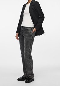 Czarna marynarka z wyraźnymi ramionami na białej dopasowanej koszuli, zestawiona z szarymi dżinsami i czarnymi masywnymi butami.