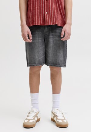 Person iført falmede svarte denimshorts, hvite crew-sokker, beige og hvite joggesko, og en rødstripet skjorte med knapper.