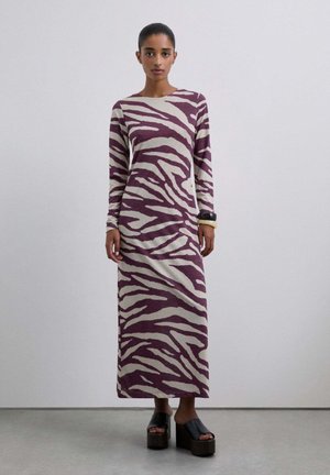 Vestido de manga larga y largo hasta el suelo en un profundo color burdeos con patrón de cebra en crema; textura suave; combinado con sandalias de plataforma negras y gruesas.