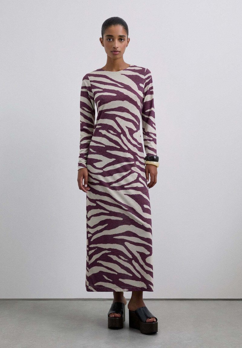 Vestido de manga larga y largo hasta el suelo en un profundo color burdeos con patrón de cebra en crema; textura suave; combinado con sandalias de plataforma negras y gruesas.