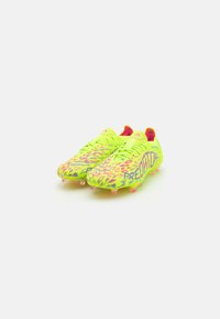 Botas de fútbol de color amarillo brillante con un patrón texturizado, acentos en rosa y la marca "PREDATOR". Diseñadas para ofrecer tracción con tacos moldeados.