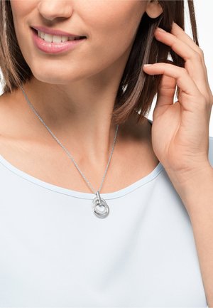 Collier en argent avec des pendentifs circulaires entrelacés, l'un ayant une surface texturée et l'autre portant des embellissements transparents.