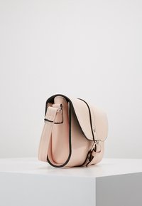 Pink syntetisk læder crossbody taske med klaplukning, sort kant og justerbar rem. Glat tekstur og rund form.