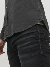 Camisa de mezclilla negra con dobladillo curvado y botones metálicos, combinada con jeans de mezclilla negra con un acabado texturizado y corte ajustado.