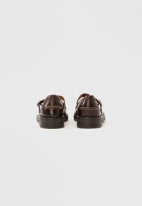 Chaussures en cuir marron à la texture lisse, avec un design à dos fermé, une couture contrastante et une semelle en caoutchouc plate.