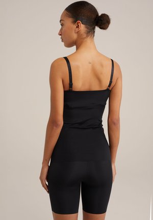 Sort ærmeløs top med justerbare stropper og tætsiddende design. Blødt, glat stof parret med sorte højtaljede shorts.