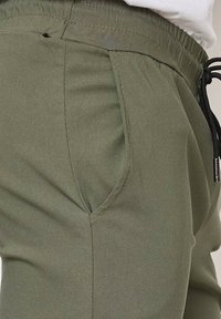 Pantalons de jogging vert olive en tissu doux, dotés de poches latérales, d'une taille élastique et d'un cordon de serrage ajustable.