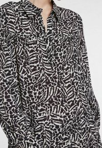 Camicia a maniche lunghe con bottoni in un motivo astratto bianco e nero. Realizzata in tessuto leggero con una vestibilità comoda e due tasche sul petto.