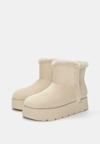 Stivali alla caviglia in platform beige realizzati in morbida suede con una finitura in pelliccia sintetica sulla parte superiore e una suola spessa e textured.