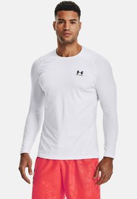 Weißes Langarm-Sportshirt mit Rundhalsausschnitt und schwarzem Under Armour-Logo auf der linken Brust, aus einem glatten, dehnbarem Stoff gefertigt.