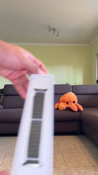 Black watch band in a white box, featuring a textured surface design and metallic hardware. Background includes a soft orange octopus plush toy.