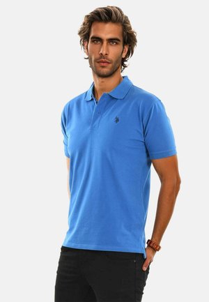 Blue polo shirt with short sleeves, collared neck, plain design, and a small dark logo on the chest. Worn with black pants.