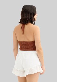 Top corto de ganchillo marrón con diseño de cuello halter, combinado con pantalones cortos blancos con volantes y detalles de ojal, de corte holgado.