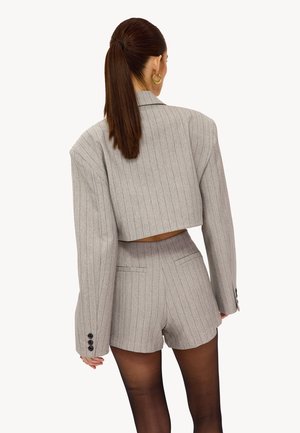 Blazer court à rayures grises avec manches larges, associé à un short taille haute assorti, avec des boutons décoratifs et un design structuré.