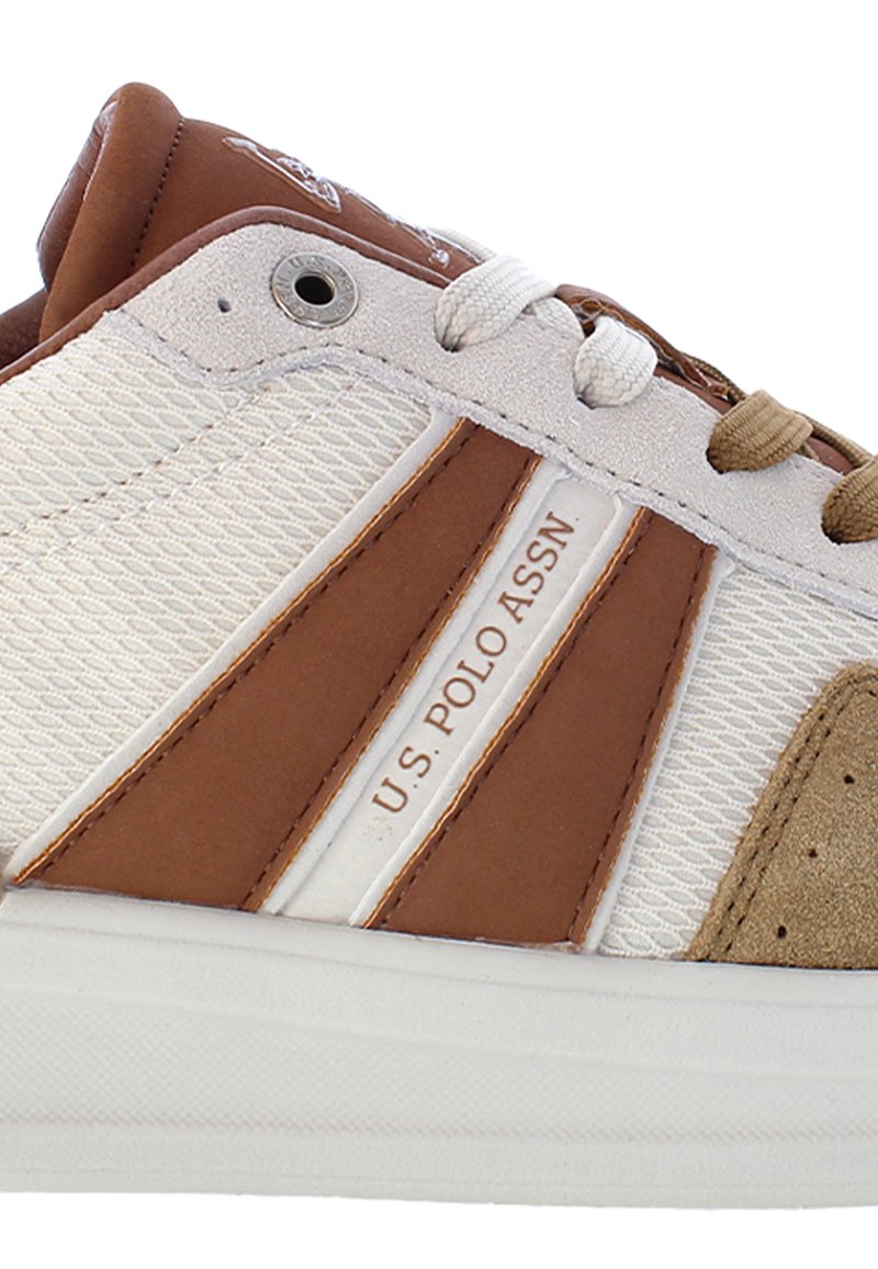 Sneaker bianca con accenti color beige e una parte superiore testurizzata. Presenta tre strisce marroni, una punta in suede e un'etichetta con logo sulla linguetta.