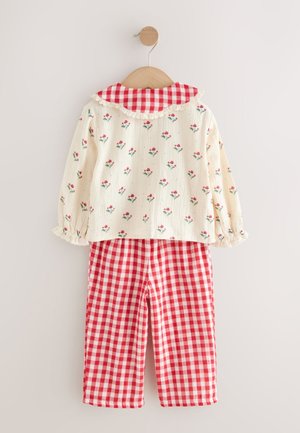 Tenue en coton avec un haut crème orné d'un imprimé floral rouge et d'un col volanté en vichy, associé à un pantalon à carreaux vichy rouge et blanc.