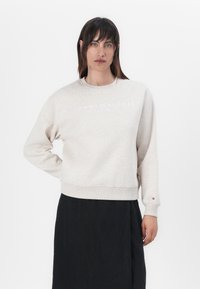 Lichtgrijze sweater met ronde hals, ribgebreide manchetten en zoom, voorzien van het witte "TOMMY HILFIGER EST. 1985" logo over de borst. Gladde textuur.