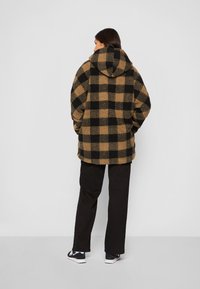 Braun und schwarz kariertes Fleece-Jacke mit Kapuze, im lässigen Schnitt und weichen Material. Getragen mit schwarzen Cargo-Hosen und Sneakers.