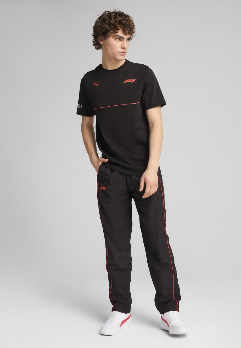 Sort t-shirt med røde accenter og logo, parret med sorte bukser med røde sidelister. Hvide sneakers fuldender looket.