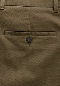 Pantalons kaki avec un tissage texturé, dotés d'une poche arrière à bouton et d'un design lisse et ajusté. La couleur est une teinte terrestre douce.