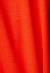 Jaskrawa czerwona tkanina o gładkiej, miękkiej fakturze, z subtelnym połyskiem i lekkim rozciągnięciem. Brak widocznych wzorów lub ozdób.