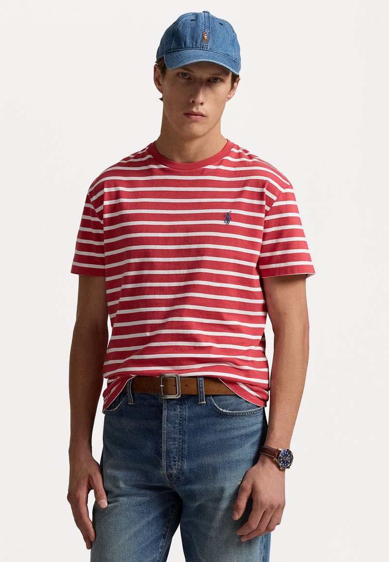 Randig t-shirt i rött och vitt, i bomullsmaterial, med rund halsringning. Buren med blå jeans och en blå denimkeps. Brunt bälte och klockdetalj.