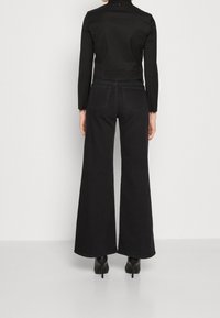 Svart vidbenad jeans gjort av denim med en slät textur. Har bakfickor och en hög midja, i kombination med klackskor.