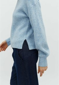 Maglione azzurro chiaro a coste con vestibilità rilassata, con fessure laterali e maniche lunghe, abbinato a pantaloni sartoriali blu navy. Tessuto morbido e design casual.