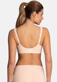 Light peach sports bra with a textured design, adjustable straps, and a hook closure at the back. Smooth fabric, minimalistic style.