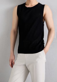 Top senza maniche nero con una texture a coste, dotato di scollatura rotonda e spacchi laterali. Abbinato a pantaloni su misura di colore chiaro.